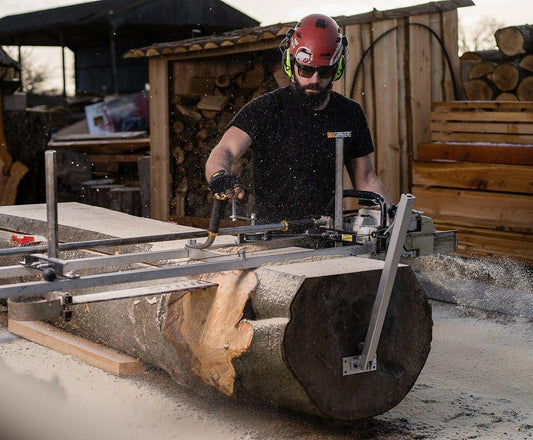 Person using a portable chainsaw mill attached to a guide rail, milling a large log with sawdust flying in the air