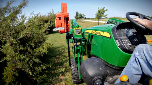 Chainsaw mounted on a compact tractor loader arm in a black SawHaul scabbard, saw upright and secure as the operator drives